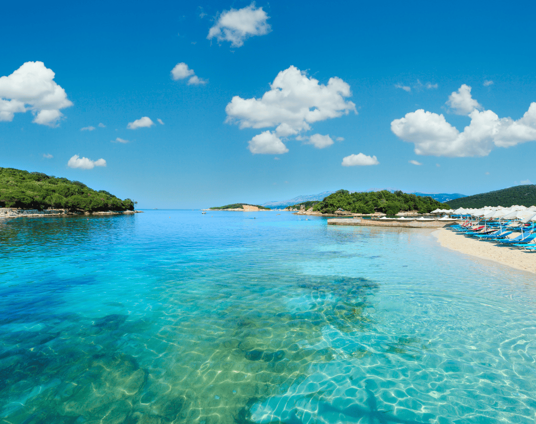Crystal-clear waters and white sandy beach in Ksamil, Albania with sunbeds and lush surroundings – budget summer travel gem in Eastern Europe