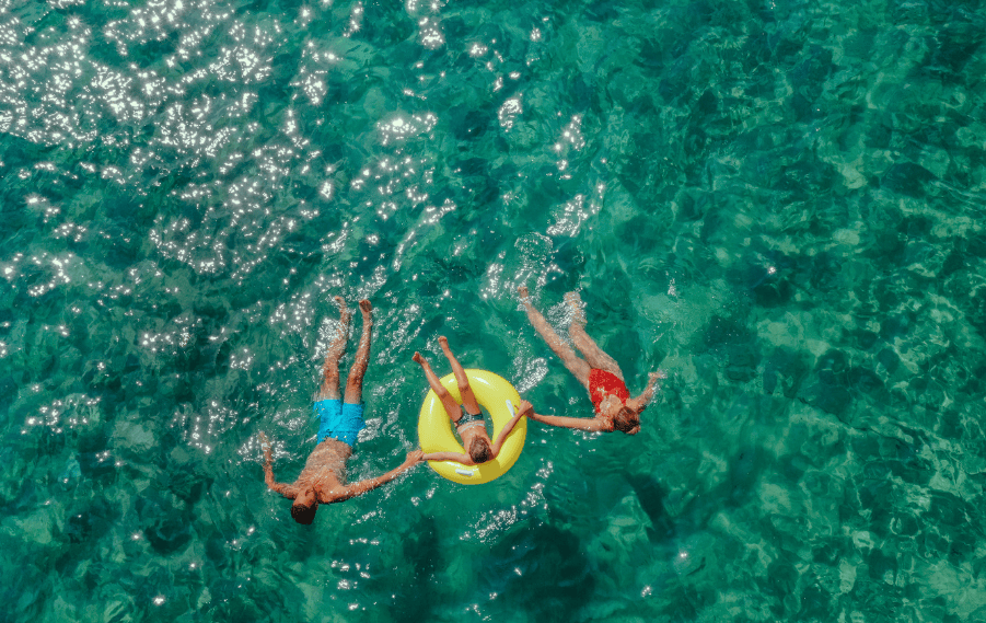 Aerial view of family swimming and floating in crystal clear turquoise sea on a summer holiday.