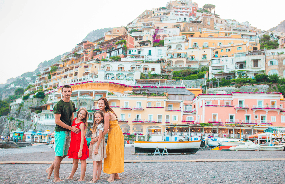 Happy family enjoying summer vacation in Positano, Italy with colorful seaside buildings in the background.