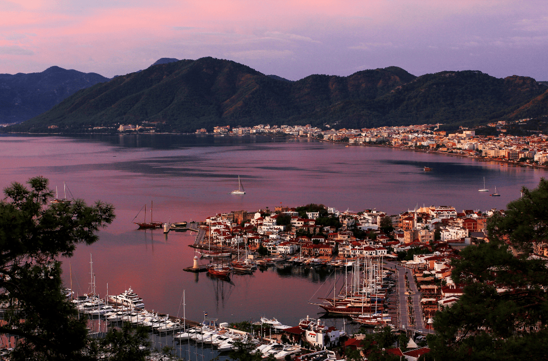 Stunning sunset view over Marmaris, Turkey, showing yachts, the harbor, and the city surrounded by forested mountains.
