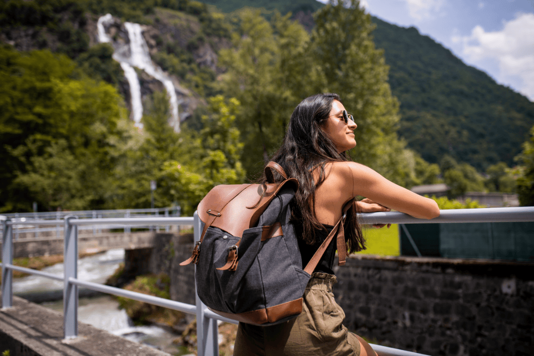 Young woman on a solo travel adventure admiring a waterfall in the European mountains during September
