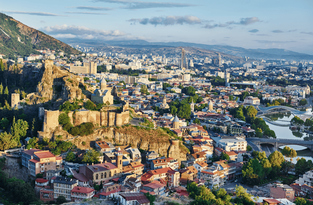 Panoramic view of Tbilisi, Georgia with Narikala Fortress, Holy Trinity Cathedral, and colorful old town buildings along the Kura River.