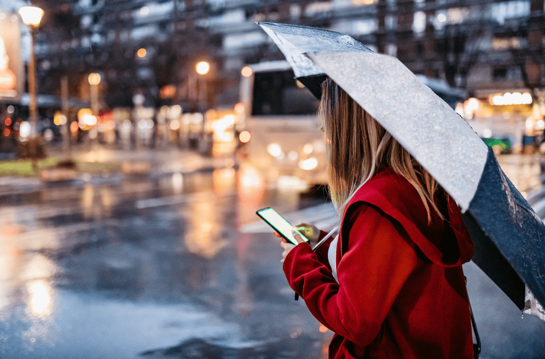 woman under rain with an umbrella with a phone on her hand